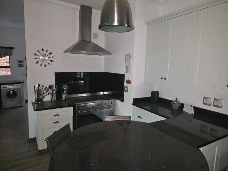 A well-maintained kitchen featuring shaker-style cabinetry, black granite countertops, a stainless steel extractor fan, and a freestanding oven with a glass splashback.