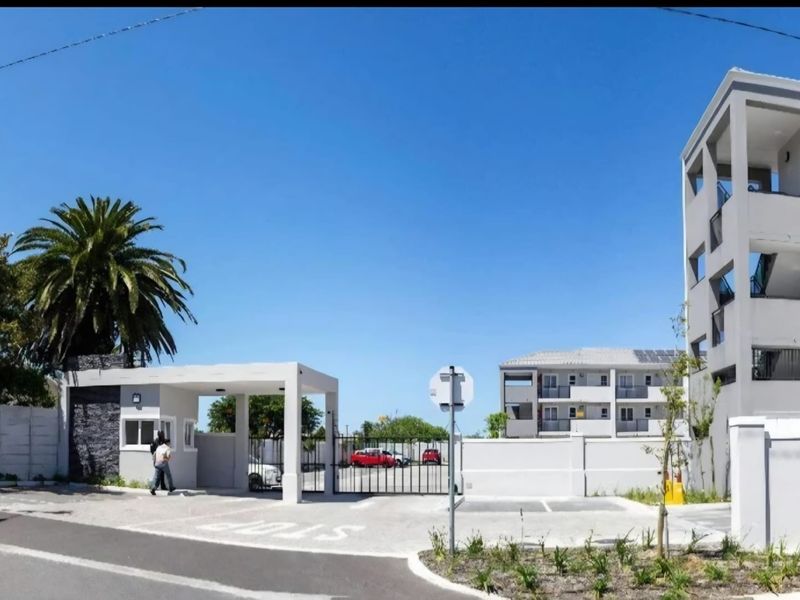 Front entrance view of a modern apartment complex featuring a secure gated access point, guard house, and paved driveway.