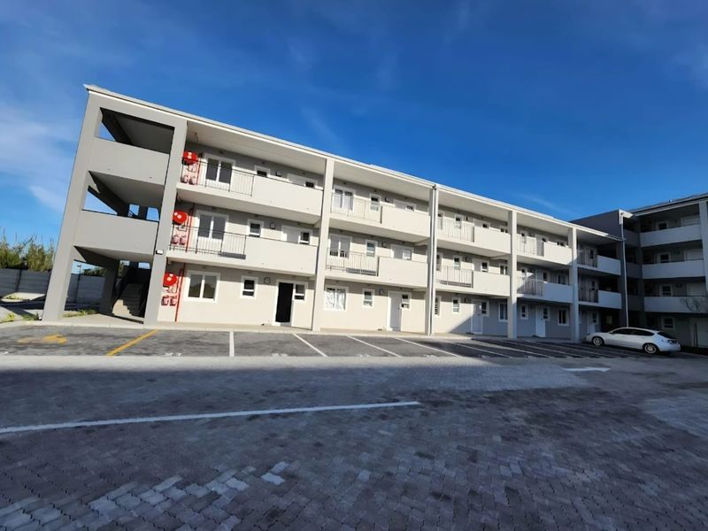 A modern multi-story apartment complex featuring paved parking, external stairwell access, and private balconies for each unit.