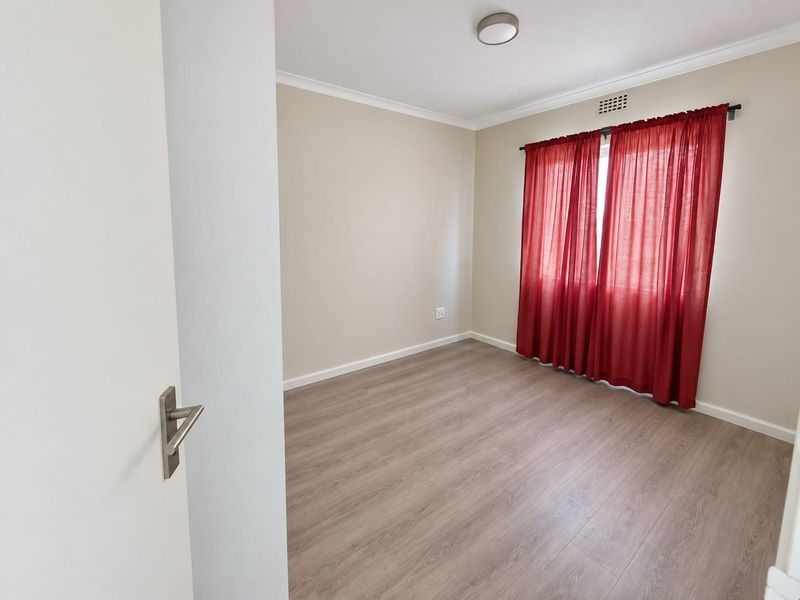 A clean, empty bedroom featuring neutral wall tones, modern laminate flooring, and a flush mount ceiling light fixture.