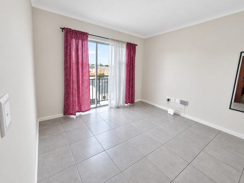 A bright, empty bedroom featuring neutral tiled flooring, cove cornicing, and a sliding glass door providing access to a private balcony.