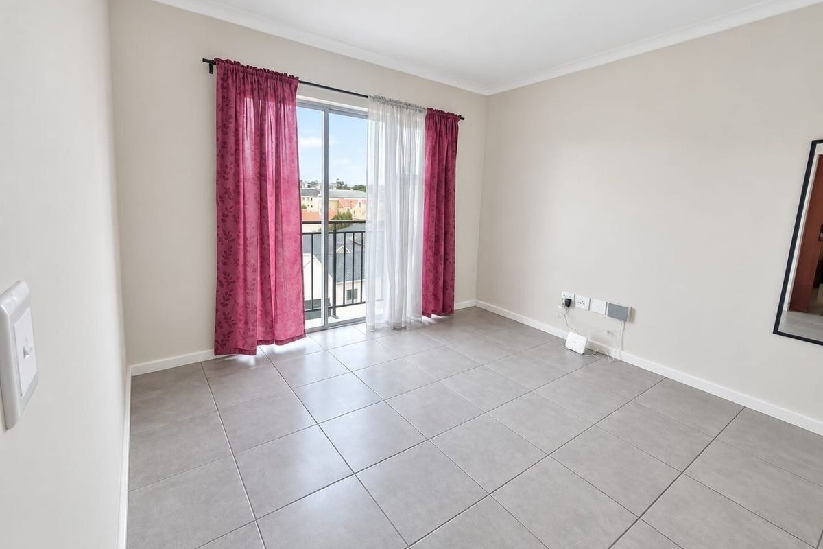 A bright, empty bedroom featuring neutral tiled flooring, cove cornicing, and a sliding glass door providing access to a private balcony.