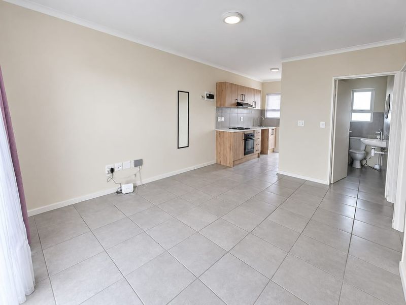 An open-plan living area featuring tiled flooring and a compact kitchen with built-in cabinetry, oven, and hob, leading to an adjacent bathroom.