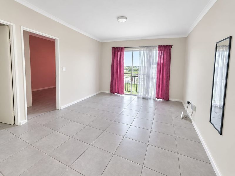 A bright, empty living room featuring neutral tiled flooring, cove cornicing, and a sliding glass door providing access to a balcony.