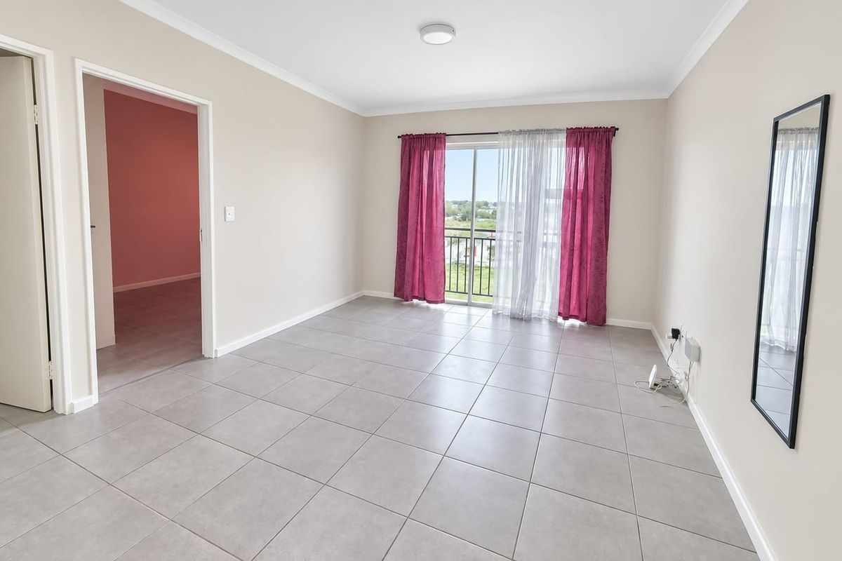 A bright, empty living room featuring neutral tiled flooring, cove cornicing, and a sliding glass door providing access to a balcony.