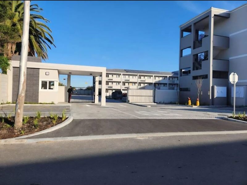 View of the apartment complex entrance featuring a security gate, guard house, and paved driveway leading to the multi-story residential building.