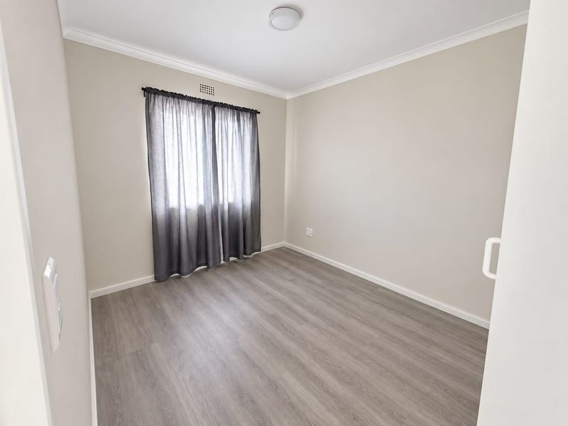 A clean, empty bedroom featuring modern grey laminate flooring, neutral walls, and a simple ceiling light fixture.