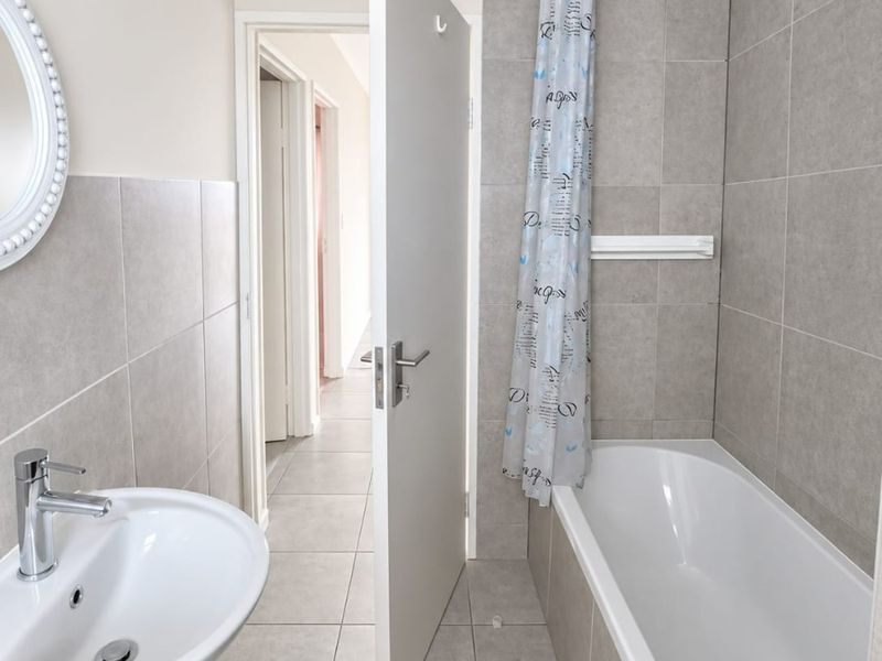 A clean, neutral-toned bathroom featuring a pedestal basin, a standard bathtub with a shower curtain rail, and modern ceramic tiling throughout.