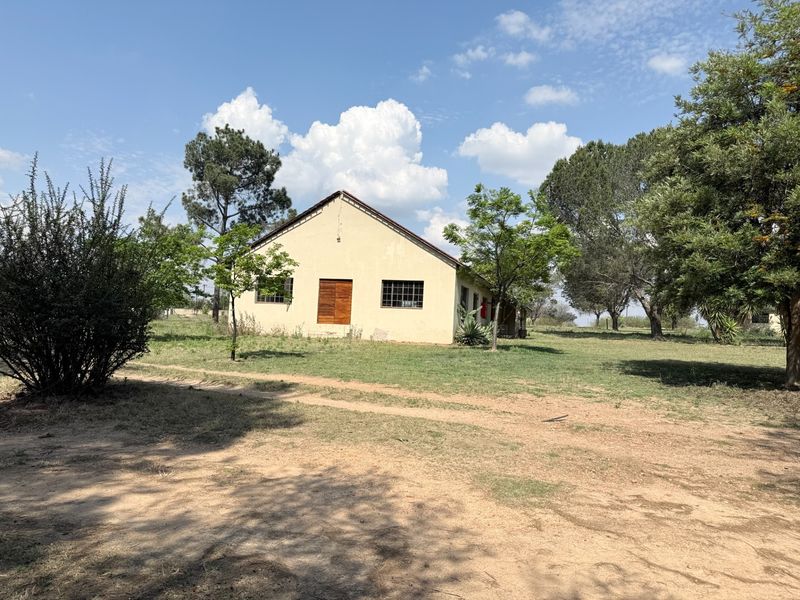 A view of the rear exterior of the farm building, featuring a pitched roof, security-barred windows, and wooden double doors set in a rural landscape.