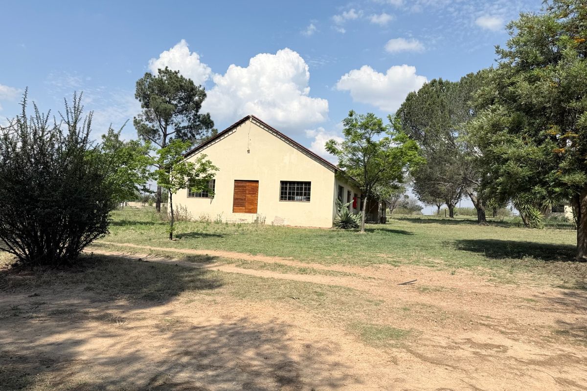 A view of the rear exterior of the farm building, featuring a pitched roof, security-barred windows, and wooden double doors set in a rural landscape.