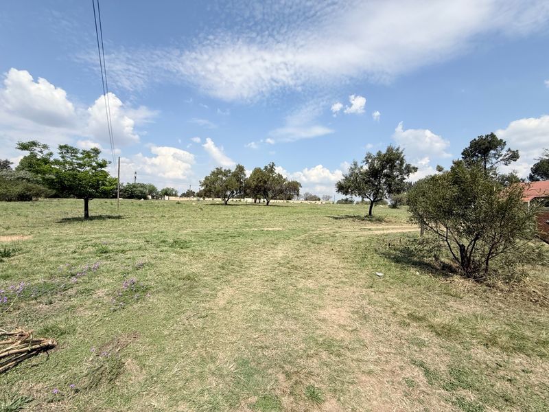 A wide, open grassy field on the farm property featuring scattered mature trees and clear blue skies.