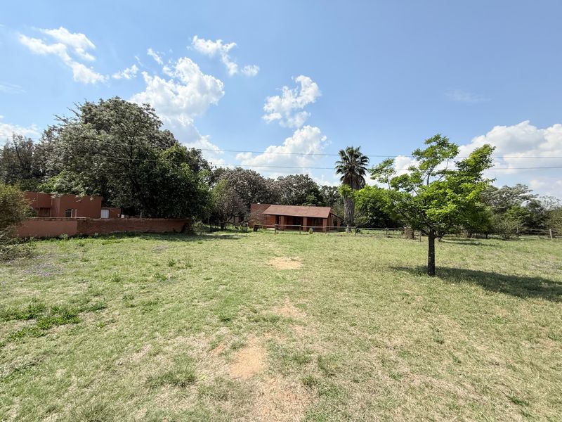 A view of the rear garden area featuring a brick boundary wall, open lawn space, and a single-story dwelling with a tiled roof.