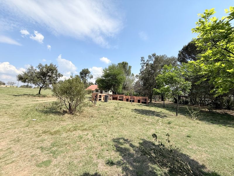 Expansive farm garden featuring a large built-in brick braai area set within a spacious, tree-lined landscape.