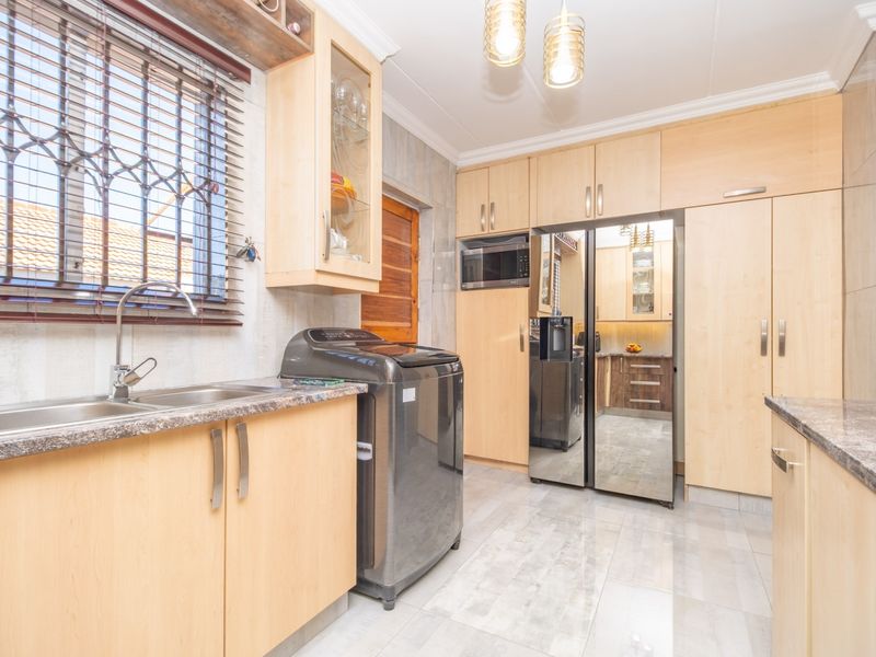 A functional kitchen featuring light wood cabinetry, laminate countertops, a stainless steel sink, and integrated microwave, with tiled flooring and ample storage space.
