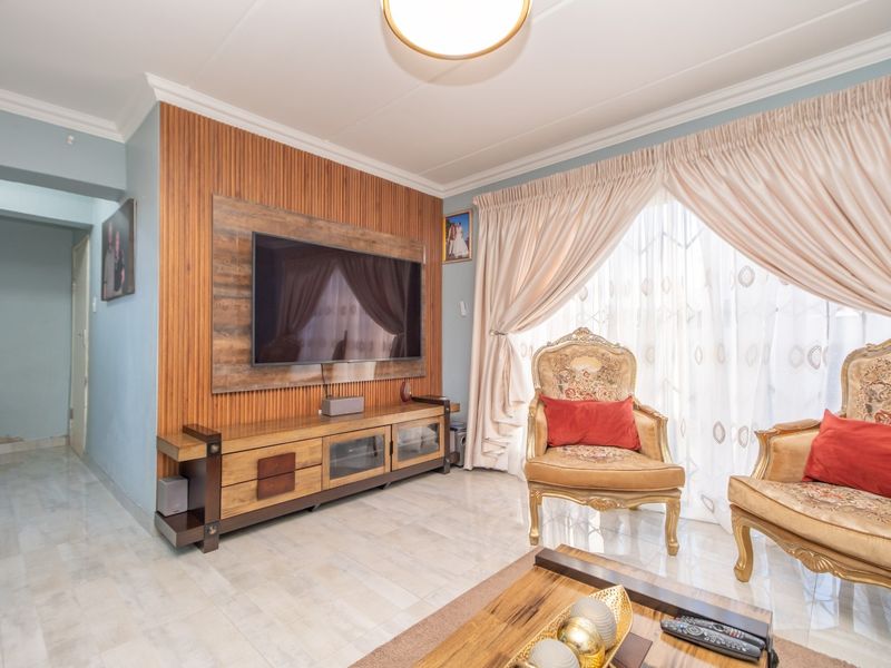 A well-maintained living room featuring a decorative wood slat feature wall, tiled flooring, and classic ceiling cornicing.