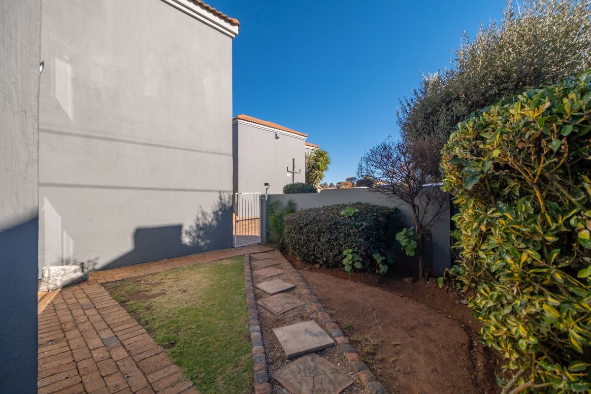 A rear exterior view showing a paved walkway, a stepped stone path, and a boundary wall with a metal gate.