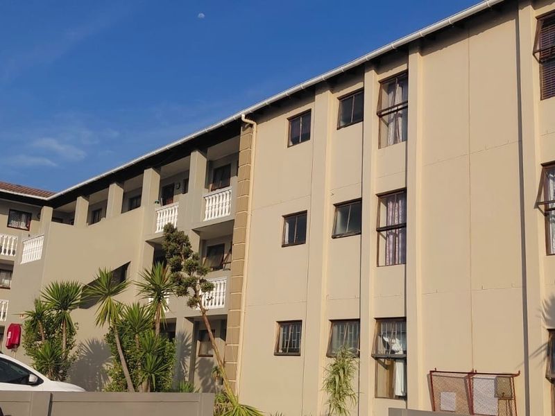Exterior view of a multi-story apartment complex featuring a neutral facade, tiled roofing, and balcony balustrades.