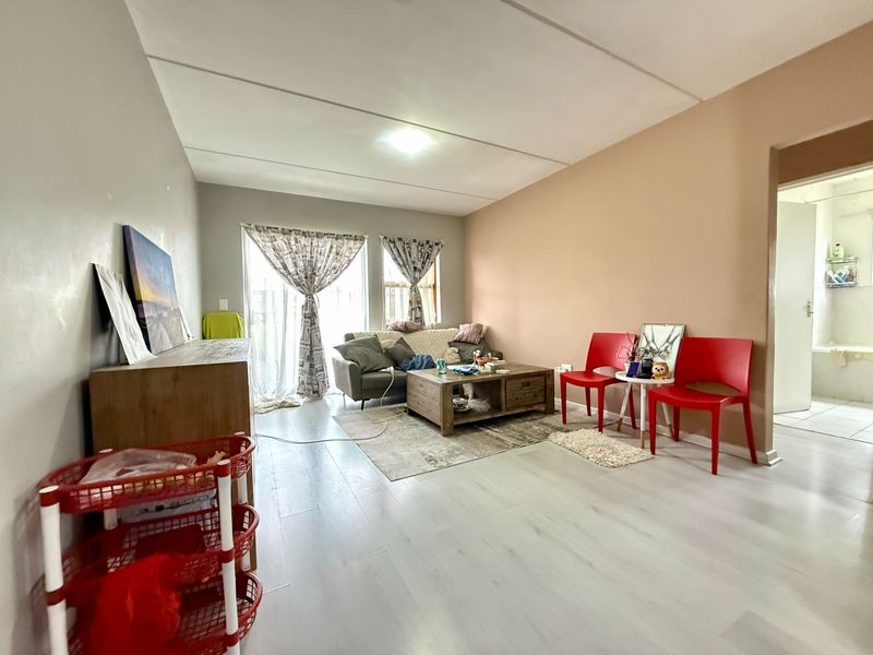 A living room featuring light-toned laminate flooring and a sliding glass door providing natural light, with an adjacent view into a bathroom.