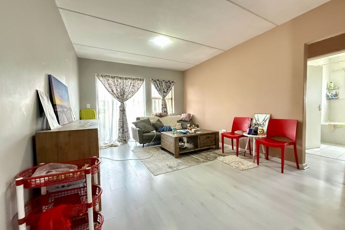A living room featuring light-toned laminate flooring and a sliding glass door providing natural light, with an adjacent view into a bathroom.