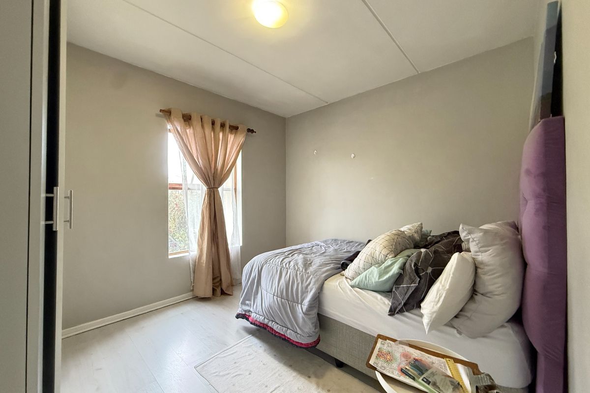 A functional bedroom featuring light-toned laminate flooring, a built-in wardrobe, and a window providing natural light.