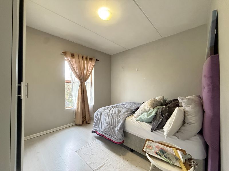 A functional bedroom featuring light-toned laminate flooring, a built-in wardrobe, and a window providing natural light.