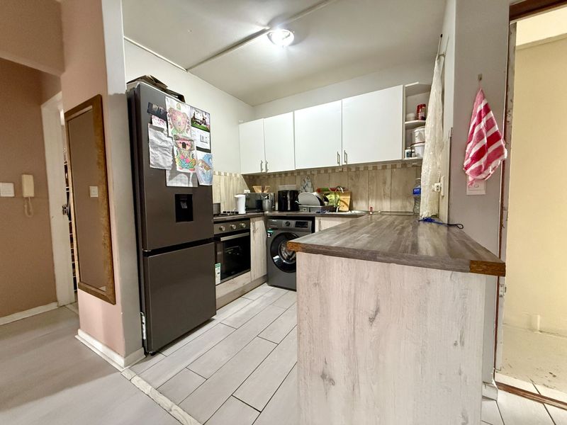 Compact kitchen featuring white cabinetry, wood-look laminate countertops, tiled backsplash, and integrated oven with hob, providing a functional cooking space.