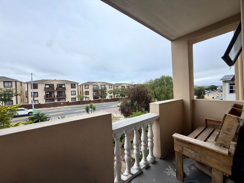 A covered balcony featuring a concrete floor and a decorative balustrade, offering an elevated view of the surrounding residential street and neighborhood.