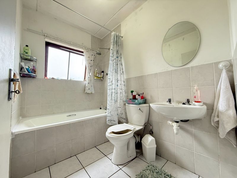 A functional bathroom featuring a built-in bathtub, wall-mounted basin, and neutral ceramic tiling, requiring cosmetic updates to improve its overall condition and aesthetic appeal.