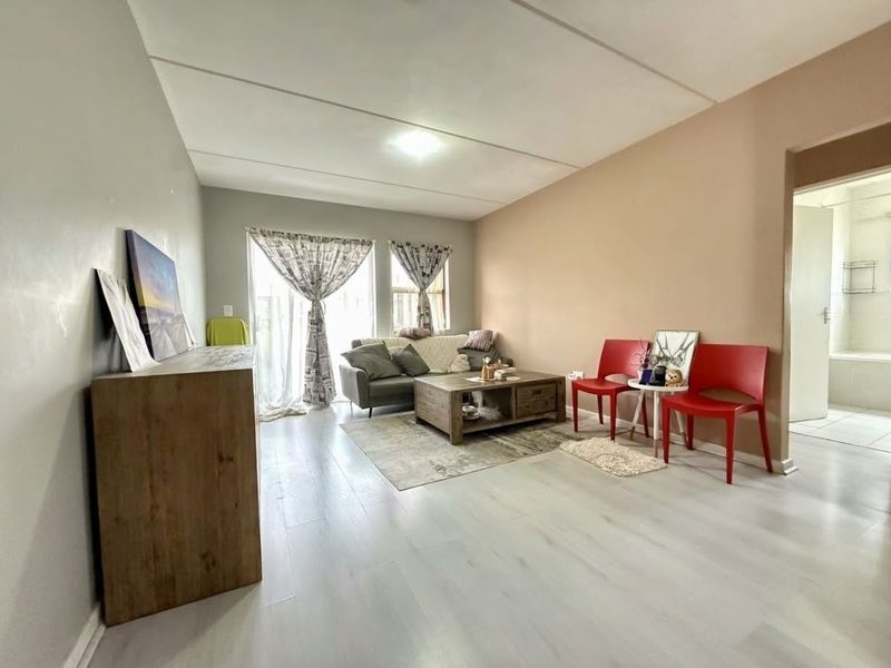 A bright living room featuring light-toned laminate flooring and a sliding glass door providing natural light.