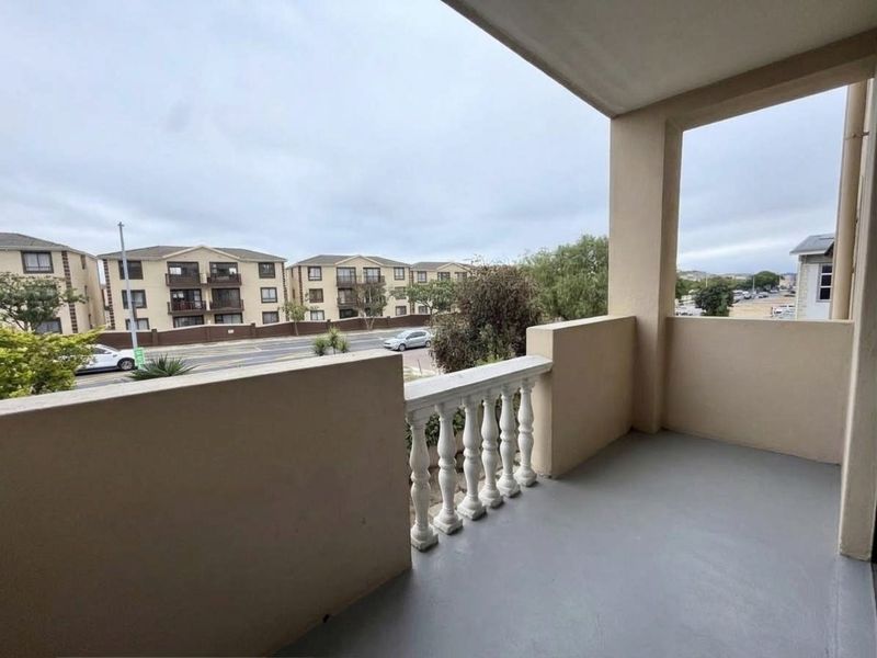 A covered balcony featuring a concrete floor and a classic balustrade, offering an open view of the surrounding apartment complex and street.