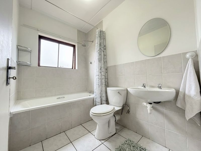 A functional bathroom featuring a bathtub with shower, wall-mounted basin, and neutral tiled finishes throughout.