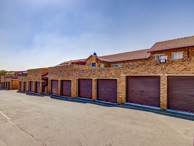A row of face brick townhouse garages featuring brown roller shutter doors and a paved driveway area.