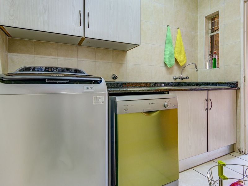 Functional laundry area featuring built-in cabinetry, granite countertops, a stainless steel sink, and tiled finishes, providing practical utility space.