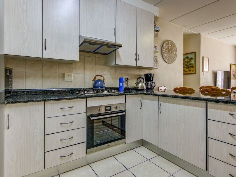 A functional kitchen featuring light wood-grain cabinetry, granite countertops, a gas hob, built-in oven, and tiled flooring, offering a practical layout for daily cooking.