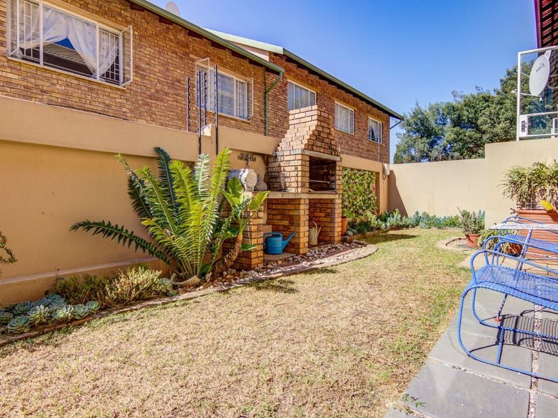 Rear garden area featuring a brick built-in braai, paved patio space, and perimeter wall with electric fencing.