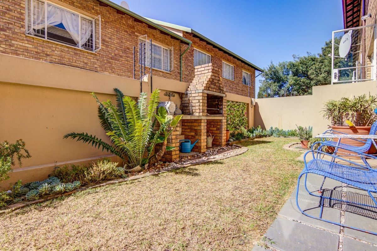 Rear garden area featuring a brick built-in braai, paved patio space, and perimeter wall with electric fencing.