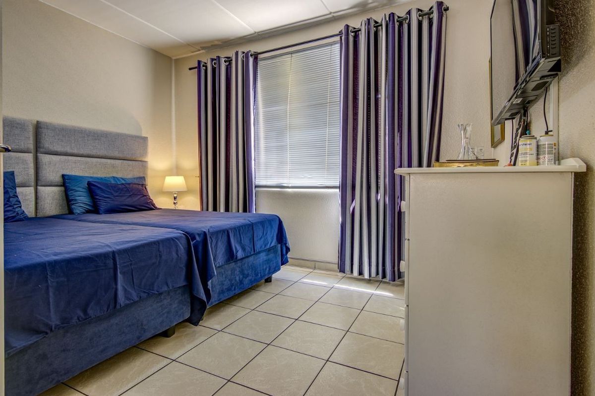 A functional bedroom featuring tiled flooring and a window with fitted blinds, providing a neutral base for potential interior updates.