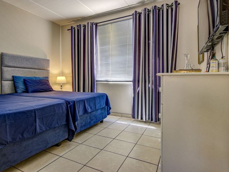 A functional bedroom featuring tiled flooring and a window with fitted blinds, providing a neutral base for potential interior updates.