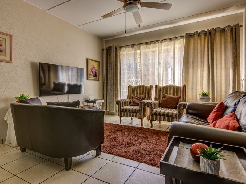 A comfortable living room featuring tiled flooring, a ceiling fan, and large windows with curtain tracks, providing a functional and well-lit space.