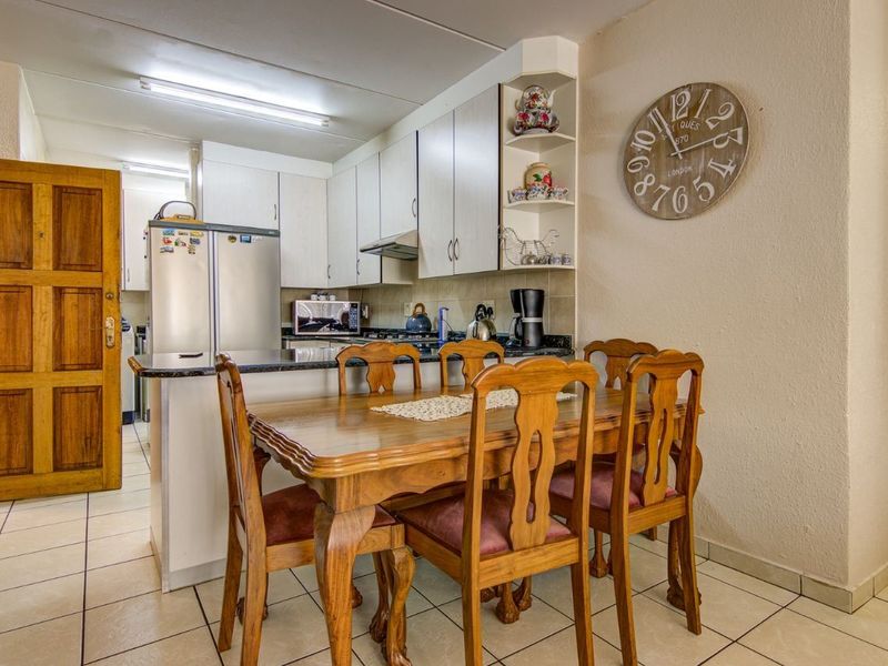 A functional kitchen featuring built-in cabinetry, granite countertops, and an extractor fan, seamlessly integrated with a dining area on tiled flooring.
