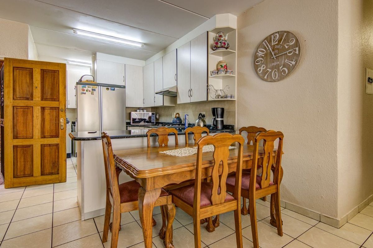 A functional kitchen featuring built-in cabinetry, granite countertops, and an extractor fan, seamlessly integrated with a dining area on tiled flooring.