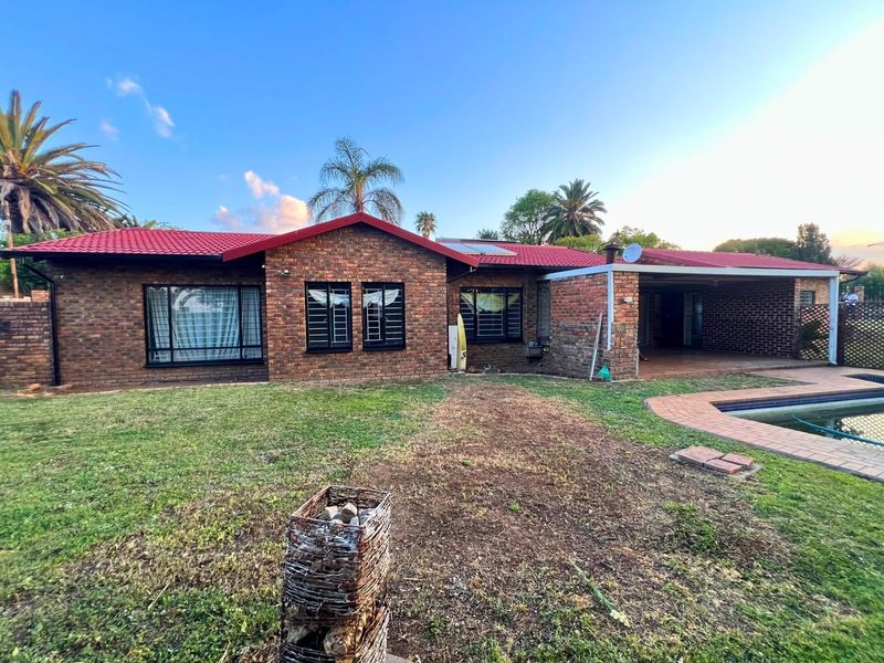 Rear view of a face brick house featuring a red metal roof, a covered patio area, and an adjacent swimming pool.