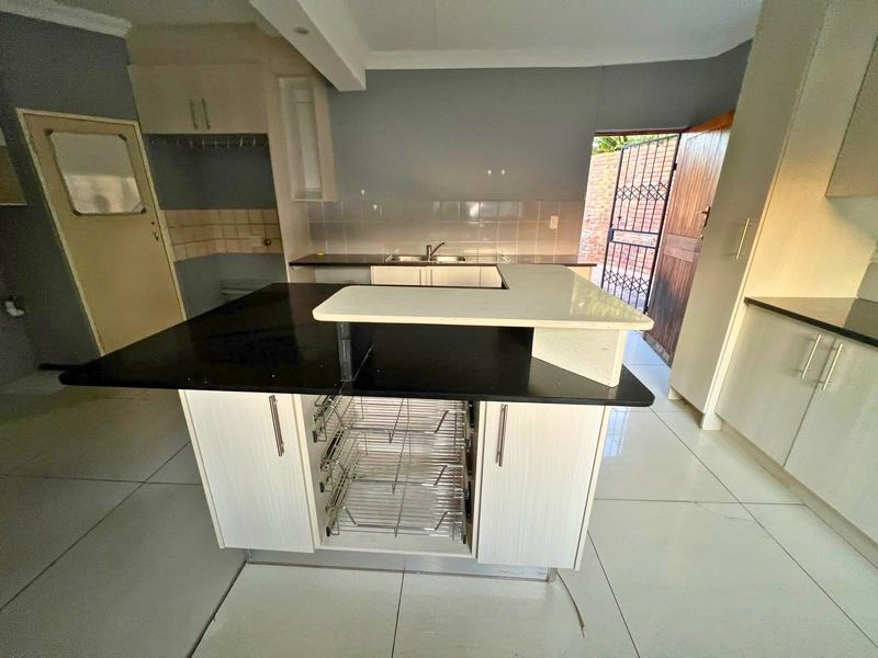 A spacious kitchen featuring a central island with stone countertops, built-in cabinetry, and tiled flooring, offering a functional layout with direct outdoor access.