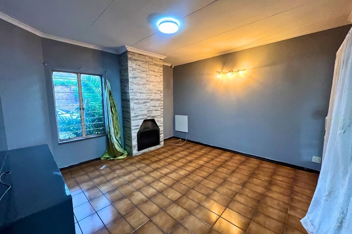 An empty living room featuring a built-in fireplace with stone-cladding detail, ceramic tiled flooring, and security bars on the window.
