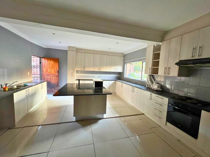 Spacious kitchen featuring a central island, ample built-in cabinetry, tiled flooring, and integrated appliances, offering a functional and clean layout.