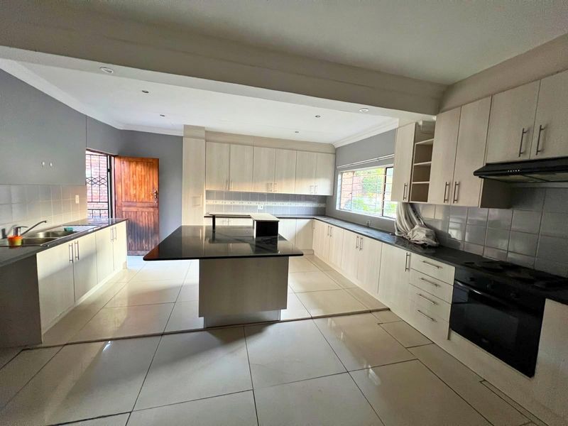 Spacious kitchen featuring a large central island, ample built-in cabinetry, integrated oven, extractor fan, and tiled flooring throughout.