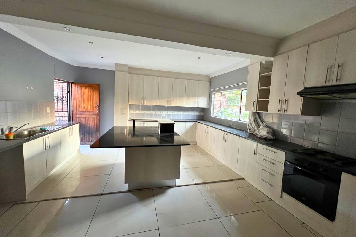 Spacious kitchen featuring a large central island, ample built-in cabinetry, integrated oven, extractor fan, and tiled flooring throughout.