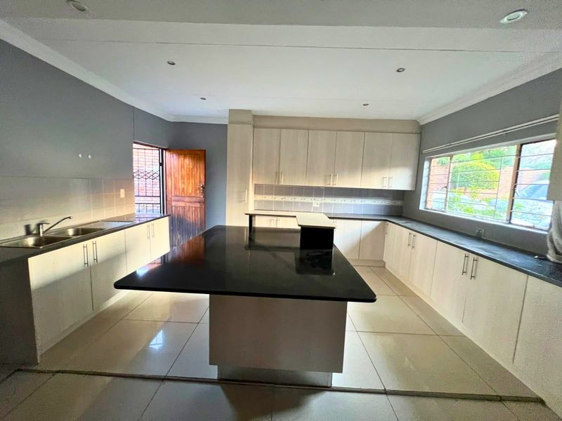 Spacious kitchen featuring a large central island with granite countertops, ample built-in cabinetry, and tiled flooring, offering a functional layout for meal preparation.