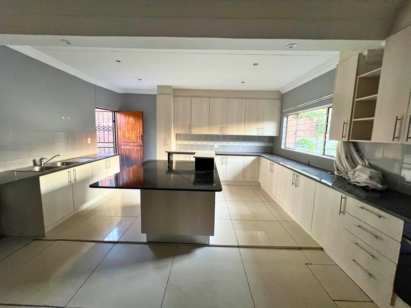 Spacious kitchen featuring a central island with granite countertops, extensive built-in cabinetry, double sink, and large format floor tiles.