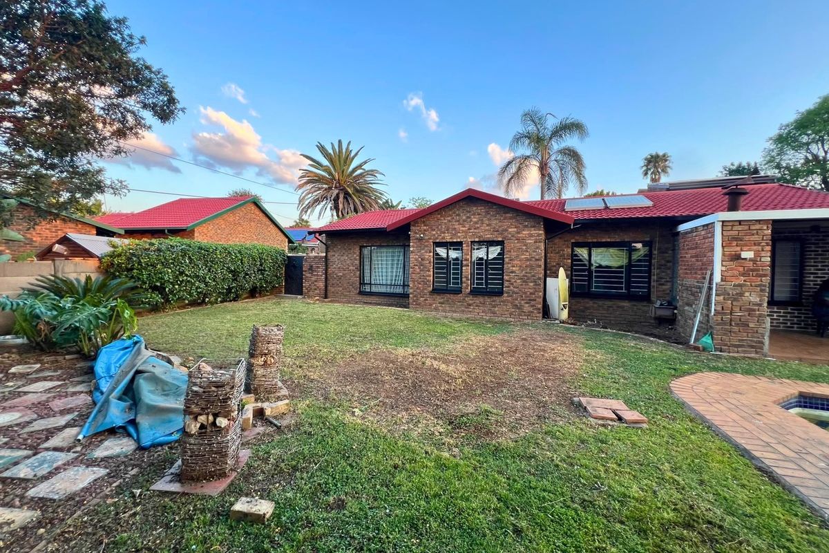 Rear view of a face brick house featuring a tiled roof, solar panels, security bars on windows, a swimming pool, and a paved patio area.